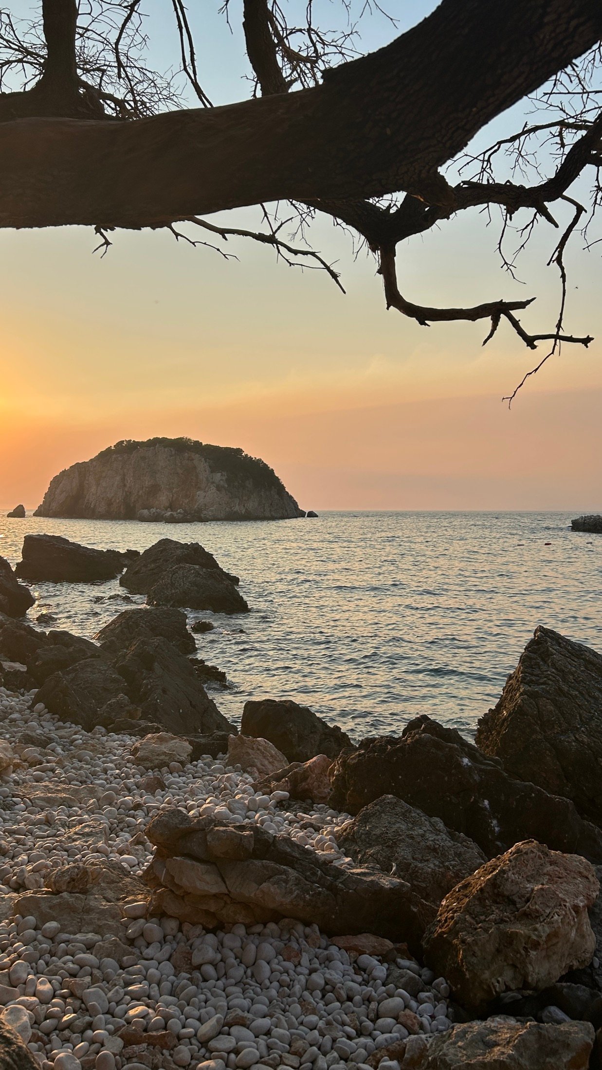 Kiesstrand mit vorgelagertem Felsen bei Sonnenuntergang